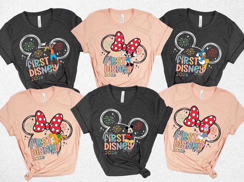 May include: A collection of six short-sleeved t-shirts in various colors, each featuring a Disney-themed graphic. The designs include Mickey Mouse ears, fireworks, and the text "First Disney Trip 2026."