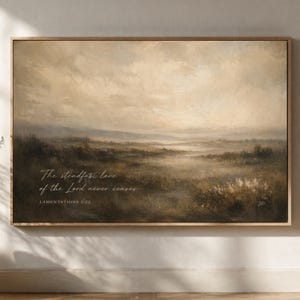 May include: Framed landscape art print with a muted color palette of browns, greens, and creams. The artwork depicts a misty field with the text "The steadfast love of the Lord never ceases. Lamentations 3:22."