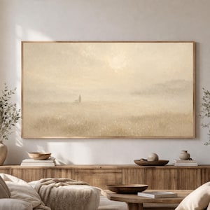 May include: A framed landscape art print in muted beige tones. The artwork depicts a solitary figure with a dog in a field, with a hazy mountain range in the background. The print is encased in a light brown wooden frame, suitable for home decor.