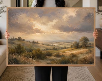 May include: A rectangular landscape painting in a light wood frame depicting a rolling countryside at sunset. The scene features golden fields, scattered green trees, and a soft, cloudy sky with warm light filtering through the horizon in muted tones.