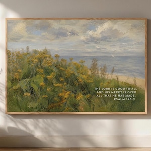 Puede incluir: Una impresión enmarcada de un paisaje costero con flores silvestres amarillas, vegetación verde y un mar en calma bajo un cielo nublado. El texto "THE LORD IS GOOD TO ALL AND HIS MERCY IS OVER ALL THAT HE HAS MADE. PSALM 145:9" es visible.