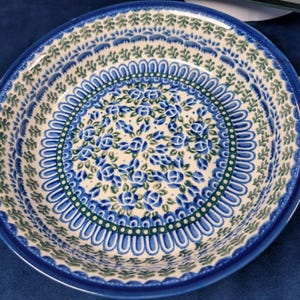 May include: Round ceramic serving bowl with blue floral pattern and two handles. The bowl features a white base with blue and green floral designs, and a dark blue rim. The handles are white with blue floral accents.