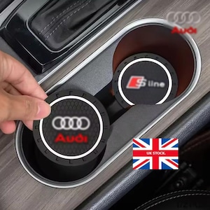 Peut inclure: Ronds de gobelet noirs pour voiture avec le logo Audi et le logo S line. Les dessous de verre sont ronds et s'insèrent dans le porte-gobelet d'une voiture. L'image montre également l'intérieur d'une voiture.