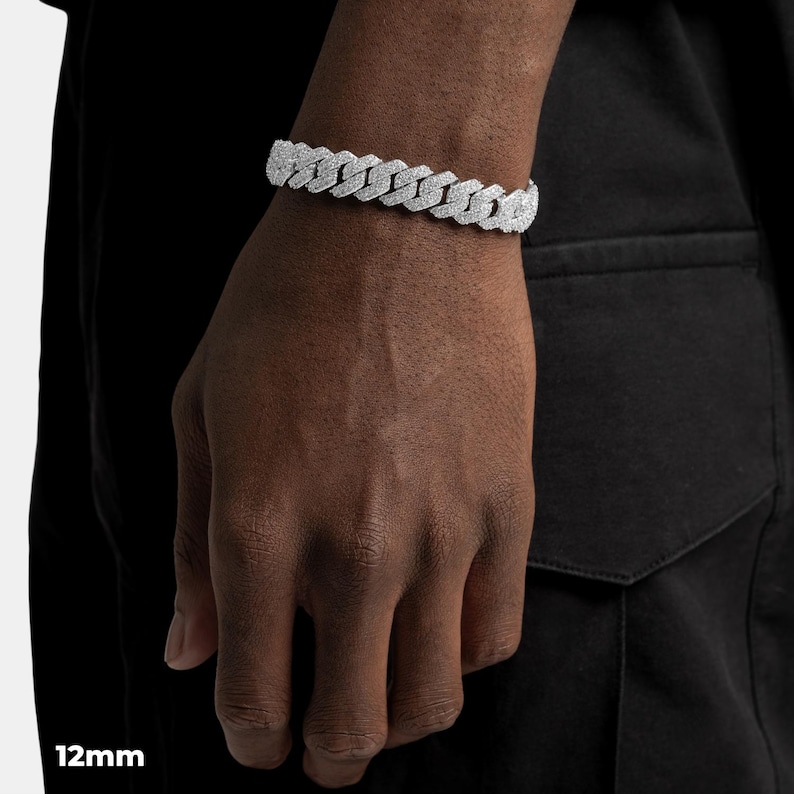 K&ouml;nnte beinhalten: Nahaufnahme eines silberfarbenen 12-mm-Armbands mit kubanischer Kette. Das Armband besteht aus mehreren ineinandergreifenden Gliedern. Das Armband befindet sich am Handgelenk einer Person, die ein schwarzes Hemd tr&auml;gt.