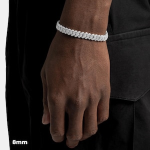 K&ouml;nnte beinhalten: Ein silberfarbenes Armband mit einer Breite von 8 mm, bestehend aus miteinander verbundenen, rechteckigen Gliedern. Das Armband ist mit kleinen, funkelnden Verzierungen versehen, die eine strukturierte Oberfl&auml;che erzeugen. Das Armband wird am Handgelenk einer Person gezeigt. Der Text "8mm" ist sichtbar.
