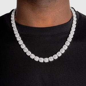 May include: A dazzling silver necklace featuring square-cut, clear gemstones. The necklace is worn against a black shirt, highlighting the sparkle of the stones. The gemstones are set closely together, creating a continuous, eye-catching design.