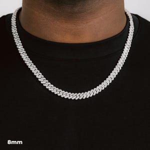 K&ouml;nnte beinhalten: Eine silberfarbene Cuban-Link-Kette mit einer Breite von 8 mm. Die Halskette besteht aus kleinen, rechteckigen Gliedern, die eng miteinander verbunden sind. Die Halskette wird um den Hals getragen und liegt auf einem schwarzen T-Shirt.