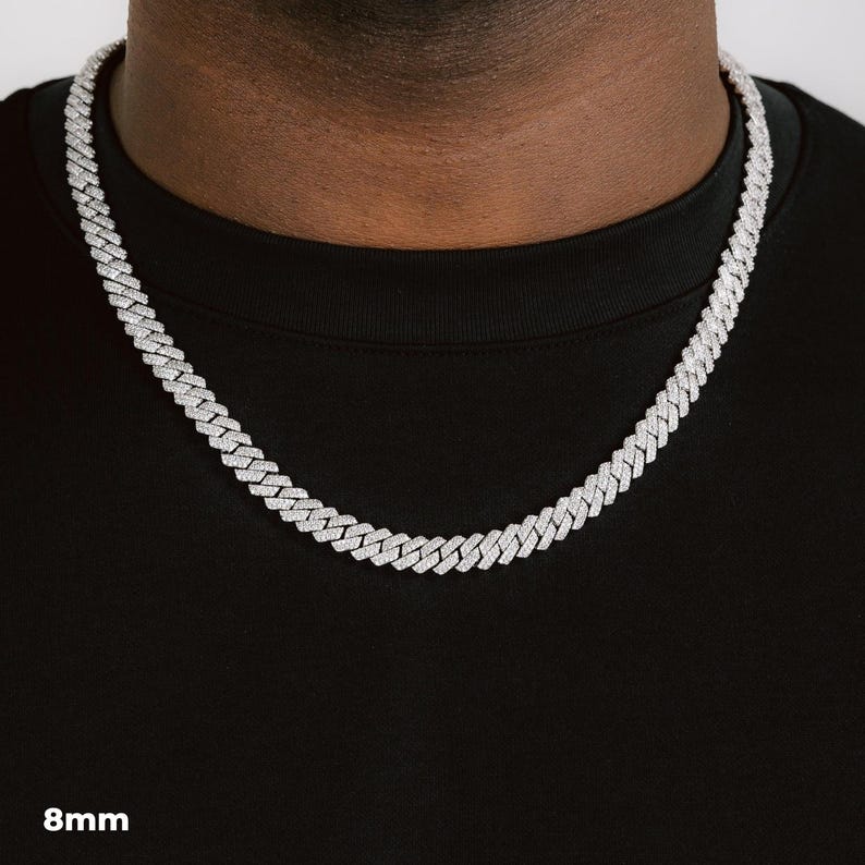 K&ouml;nnte beinhalten: Eine silberfarbene Cuban-Link-Kette mit einer Breite von 8 mm. Die Halskette besteht aus kleinen, rechteckigen Gliedern, die eng miteinander verbunden sind. Die Halskette wird um den Hals getragen und liegt auf einem schwarzen T-Shirt.