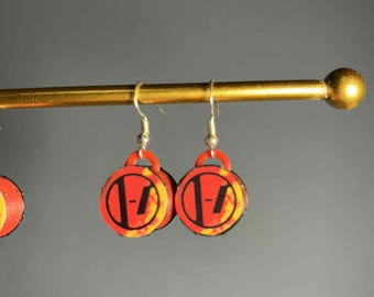 May include: A pair of round earrings with a red and yellow flame design and a black logo. The earrings are hanging from silver hooks on a gold bar. The earrings are a music-themed accessory.