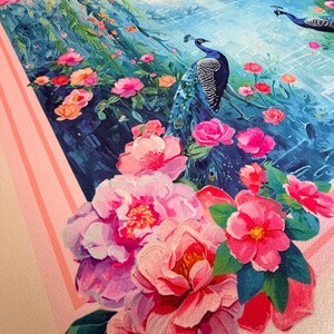 May include: A decorative textile featuring a vibrant floral and peacock design. The artwork showcases pink and red flowers, lush greenery, and two blue peacocks against a backdrop of a blue landscape. The border is a light pink with stripes.