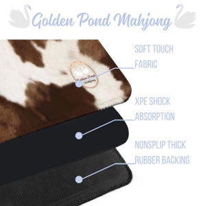 May include: A layered product with a cowhide pattern top, black middle layer, and a textured black bottom. The text "Golden Pond Mahjong" is at the top, with labels for "Soft Touch Fabric", "XPE Shock Absorption", and "Nonslip Thick Rubber Backing".