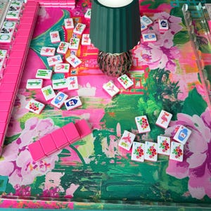 Peut inclure: Un jeu de Mahjong avec des tuiles roses et un tapis de jeu &agrave; motifs floraux dans des tons de rose et de vert. Une lampe vert fonc&eacute; avec un bouton d'alimentation est plac&eacute;e au centre. Le jeu comprend des supports en acrylique transparent.
