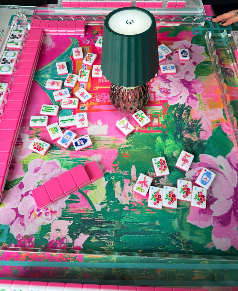 Peut inclure: Un jeu de Mahjong avec des tuiles roses et un tapis de jeu &agrave; motifs floraux dans des tons de rose et de vert. Une lampe vert fonc&eacute; avec un bouton d'alimentation est plac&eacute;e au centre. Le jeu comprend des supports en acrylique transparent.
