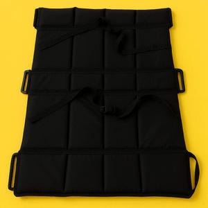 May include: Black padded seat protector with straps and buckles. The rectangular protector features vertical stitching, forming a grid. Straps are designed to secure the protector to a seat. Measurements are in centimeters.