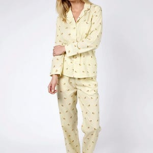 May include: A light yellow pajama set with a small, repeating floral pattern. The set includes a button-down shirt and matching pants. The pajamas are made of a soft fabric and are suitable for sleepwear.