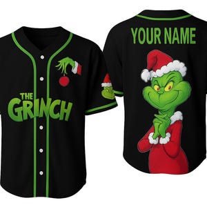May include: Black baseball jersey featuring the Grinch. The front displays "THE GRINCH" in green lettering. The back has a Grinch graphic and "YOUR NAME" in green. Green and white accents trim the collar and sleeves.