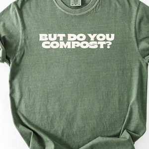May include: Green t-shirt with the text "BUT DO YOU COMPOST?" in white block letters. The shirt has a crew neck and short sleeves. The fabric appears to be a soft, slightly faded material.