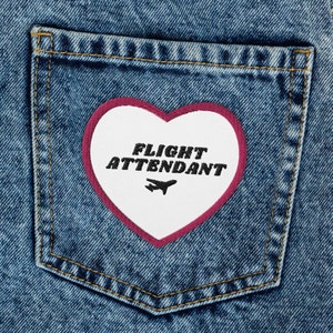 May include: A white heart-shaped patch with a pink border, sewn onto a blue denim pocket. The patch says "FLIGHT ATTENDANT" in black text with a small airplane icon.