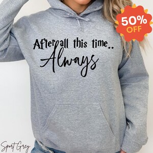 May include: A light grey hooded sweatshirt featuring a front kangaroo pocket and long sleeves. The chest displays black text that reads After all this time.. Always. The garment is made of a soft fabric and includes a drawstring hood.