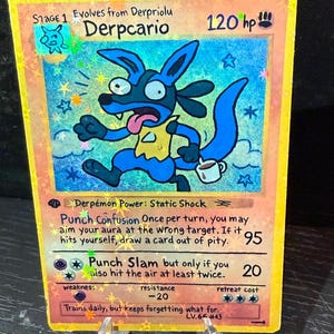 May include: A custom-illustrated trading card featuring a blue cartoon character with a long tongue and a coffee cup. The card has the name "Derpcario" and text that reads "Punch Confusion" and "Punch Slam". The card is on a clear stand.