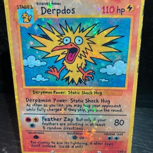 May include: A holographic trading card featuring a cartoonish yellow bird-like creature named "Derpdos." The card has a blue and yellow background with text describing the creature's abilities and stats, including "Feather Zap" and "110 hp."
