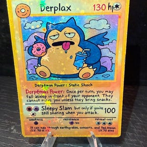 May include: A holographic trading card featuring a cartoon character named Derplax. The character is blue and tan, holding a drink and a donut. The card has text including "Sleepy Slam" and "130 hp".