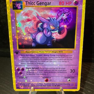 Puede incluir: Carta coleccionable holográfica con "Thicc Gengar" y 80 PS. La tarjeta tiene un esquema de color púrpura y amarillo con una ilustración de dibujos animados de un Gengar púrpura. La tarjeta incluye texto como "Stage 2" y "Booty Curse".