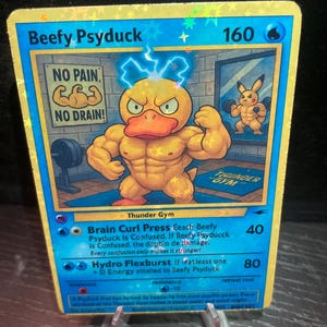 Puede incluir: Una tarjeta coleccionable holográfica con un personaje Psyduck musculoso con el texto "Beefy Psyduck". La tarjeta tiene un borde azul e incluye el texto "NO PAIN, NO DRAIN!" y "Thunder Gym".