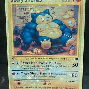 May include: A holographic 1st Edition "Beefy Snorlax" Pokémon card. The card features a muscular Snorlax character lifting weights, with a Psyduck in the background. Text includes "Rest Days Are Training Too" and card details.