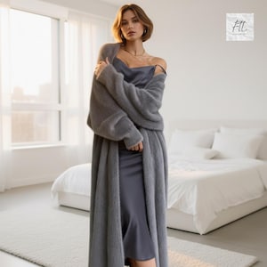 May include: A long, fuzzy, charcoal gray open-front cardigan made of a soft, textured knit material, worn over a smooth, dark gray satin slip dress with thin straps. The ensemble features a monochromatic color palette and a layered silhouette.