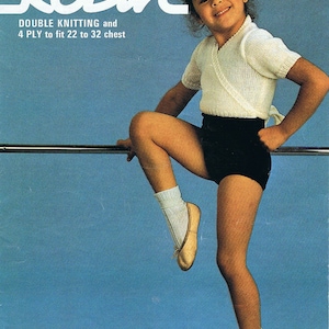 May include: A girl wearing a white knit top with a wrap style neckline and black shorts. She is standing on one leg with her other leg raised and bent at the knee. She is wearing white socks and brown ballet flats. The background is a light blue color. The text "Robin" is written in white at the top of the image. The text "Double Knitting and 4 PLY to fit 22 to 32 chest" is written in white below the word "Robin". The number "2946" is written in white in the top right corner of the image.
