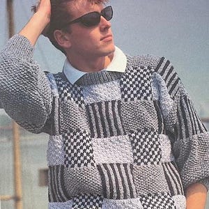Könnte beinhalten: Ein grauer und schwarzer Pullover mit einem weißen Kragen. Der Pullover hat ein geometrisches Muster mit Quadraten und Streifen.