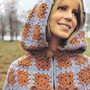 Puede incluir: Una capa con capucha de ganchillo con un patrón geométrico marrón y morado. La capa tiene un cierre de corbata en el cuello.