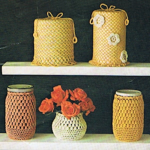May include: A display of handmade crochet items, including two cylindrical covers with handles, one with floral accents, and two jar covers. A vase with orange roses sits between the jar covers. The items are in shades of yellow and peach.