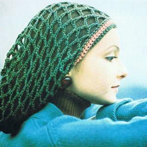 May include: A green crochet hair net with a pink trim. The net is worn by a person with brown hair. The person is wearing a blue turtleneck sweater.