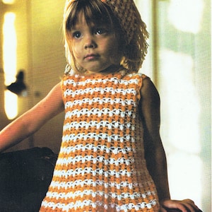 Può includere: Una bambina che indossa un vestito a crochet a righe bianche e arancioni con un cappello a crochet abbinato. Il vestito è senza maniche e ha una gonna svasata.