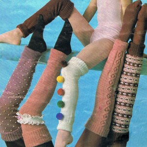 Könnte beinhalten: Vier Paar gestrickte Beinstulpen in verschiedenen Farben und Mustern. Ein Paar ist weiß mit bunten Bommeln, eines ist braun, eines ist rosa mit weißen Punkten und eines ist rosa mit einem Zopfmuster.