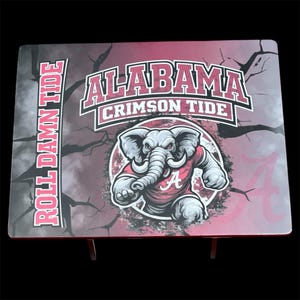 Könnte beinhalten: Ein rechteckiger Tisch mit dem Logo der Alabama Crimson Tide. Der Tisch hat einen weinroten und grauen Hintergrund mit den Worten "Roll Damn Tide" auf der linken Seite. Das Crimson Tide-Logo zeigt einen Elefanten mit einem Trikot mit dem Buchstaben "A".