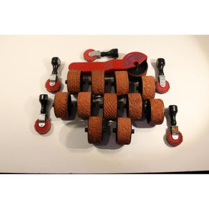 May include: A set of red and black craft tools with various patterned rolling stamps. The set includes a red handle with a circular stamp and several brown rolling stamps with different textures and designs. Additional small stamps are also included.
