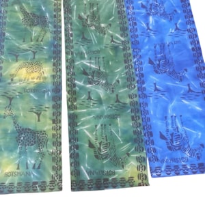 Könnte beinhalten: Drei farbenfrohe Stoffbahnen mit Tierdrucken. Eine Bahn ist grün mit Giraffen, eine weitere grün mit Zebras und die dritte blau mit Zebras. Das Wort "BOTSWANA" ist auf jeder Bahn aufgedruckt.