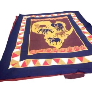 Puede incluir: Textil rectangular con un mapa de África en amarillo y marrón, con siluetas de animales. El borde es azul marino con un patrón repetitivo de triángulos rojos, blancos y amarillos. Probablemente sea una manta o un cubrecama.