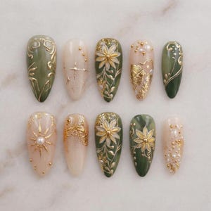 May include: A set of ten almond-shaped artificial nails with various designs. The nails feature a color palette of olive green, cream, and gold. Designs include floral patterns, gold leaf accents, and pearl embellishments, offering a sophisticated and artistic aesthetic.