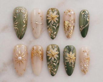 May include: A set of ten almond-shaped artificial nails with various designs. The nails feature a color palette of olive green, cream, and gold. Designs include floral patterns, gold leaf accents, and pearl embellishments, offering a sophisticated and artistic aesthetic.