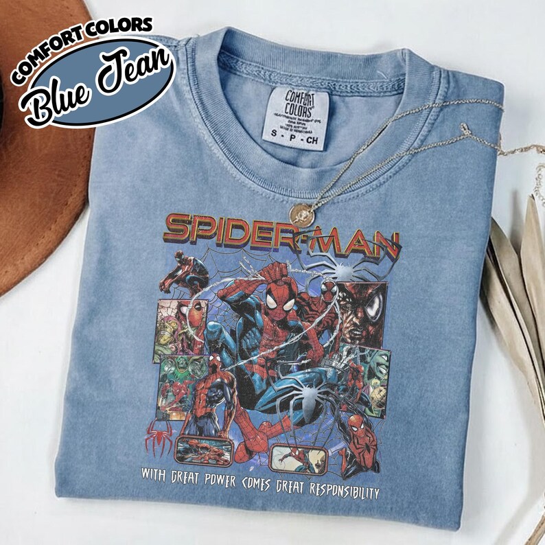 K&ouml;nnte beinhalten: Ein blaues Comfort Colors T-Shirt mit einem Spider-Man-Motiv. Die Grafik enth&auml;lt das Wort "SPIDERMAN" und den Satz "WITH GREAT POWER COMES GREAT RESPONSIBILITY". Das Shirt hat einen Rundhalsausschnitt und kurze &Auml;rmel.