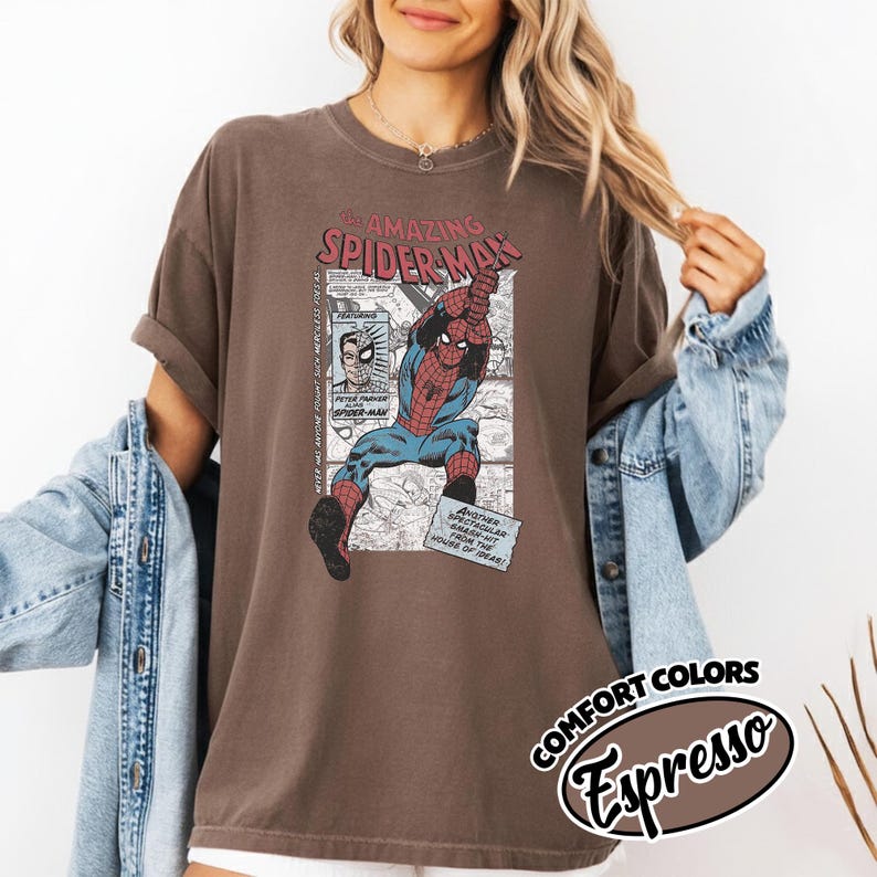K&ouml;nnte beinhalten: Espressofarbenes T-Shirt mit einer Comic-Grafik von Spider-Man. Das Design enth&auml;lt den Text "The Amazing Spider-Man" und andere Comic-Elemente. Teil der Comfort Colors-Kollektion.