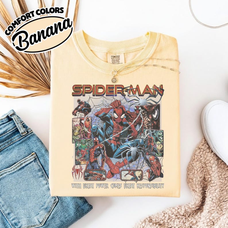 K&ouml;nnte beinhalten: Ein hellgelbes T-Shirt mit einem Spider-Man-Motiv. Die Grafik zeigt das Wort "Spider-Man" in Rot und eine Collage von Spider-Man-Illustrationen. Der Text "WITH GREAT POWER COMES GREAT RESPONSIBILITY" ist ebenfalls sichtbar.
