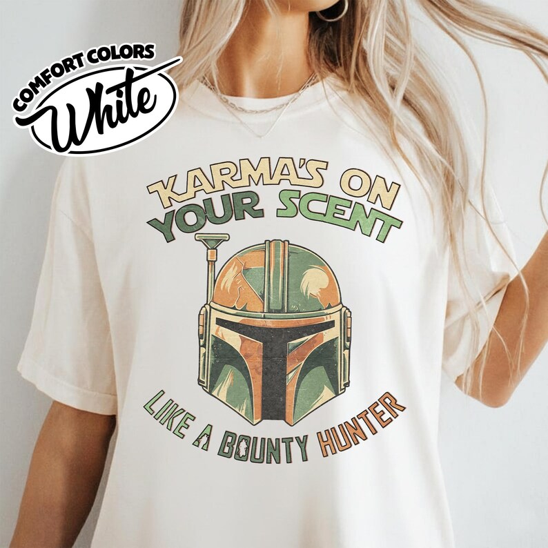 May include: White Comfort Colors t-shirt featuring a graphic of a Mandalorian helmet with the text "Karma's on Your Scent Like a Bounty Hunter" in green and orange. The shirt has a relaxed fit.