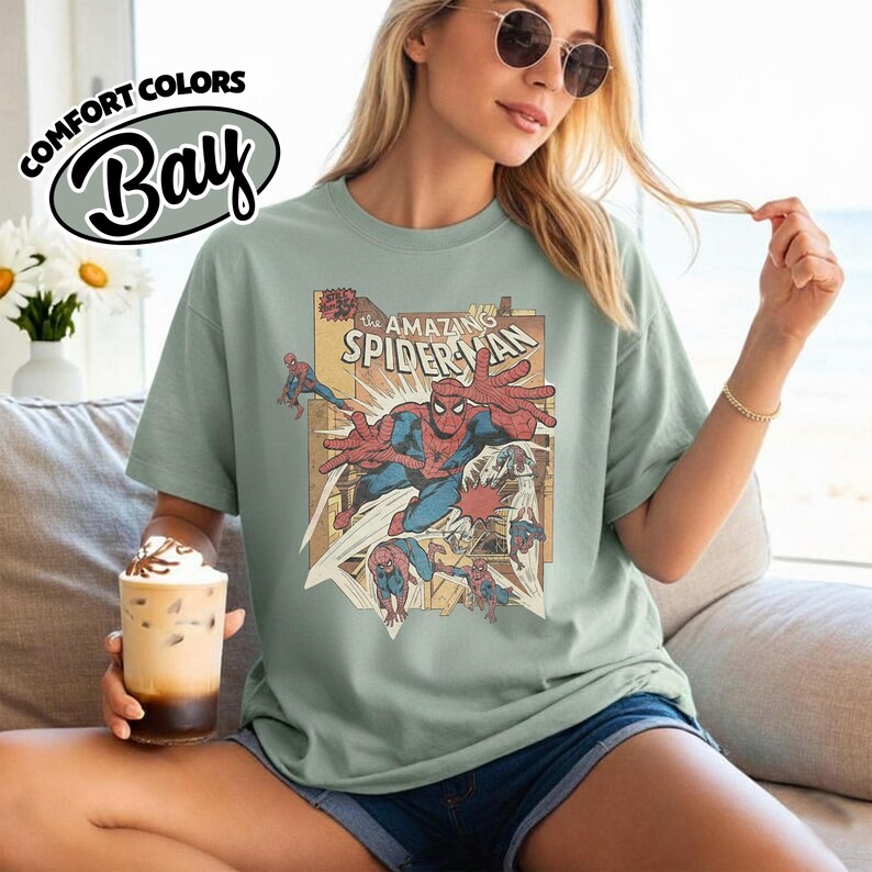 K&ouml;nnte beinhalten: Hellgr&uuml;nes T-Shirt mit einem Vintage-Comic-Grafik von Spider-Man. Die Grafik enth&auml;lt den Text "The Amazing Spider-Man" und Actionposen des Superhelden. Das Shirt ist von der Marke Comfort Colors.