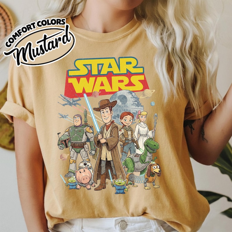 May include: Mustard-colored t-shirt featuring a Star Wars graphic with characters from Toy Story. The design includes Woody as a Jedi, Buzz Lightyear, and other characters. The words "COMFORT COLORS" and "Mustard" are printed on the top left.