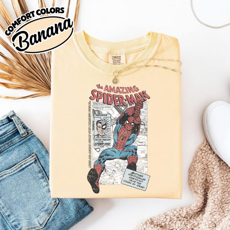 K&ouml;nnte beinhalten: Hellgelbes T-Shirt mit einer Grafik von Spider-Man in Aktion, mit dem Text "The Amazing Spider-Man". Das Shirt tr&auml;gt auch die Aufschrift "Comfort Colors" und "Banana".